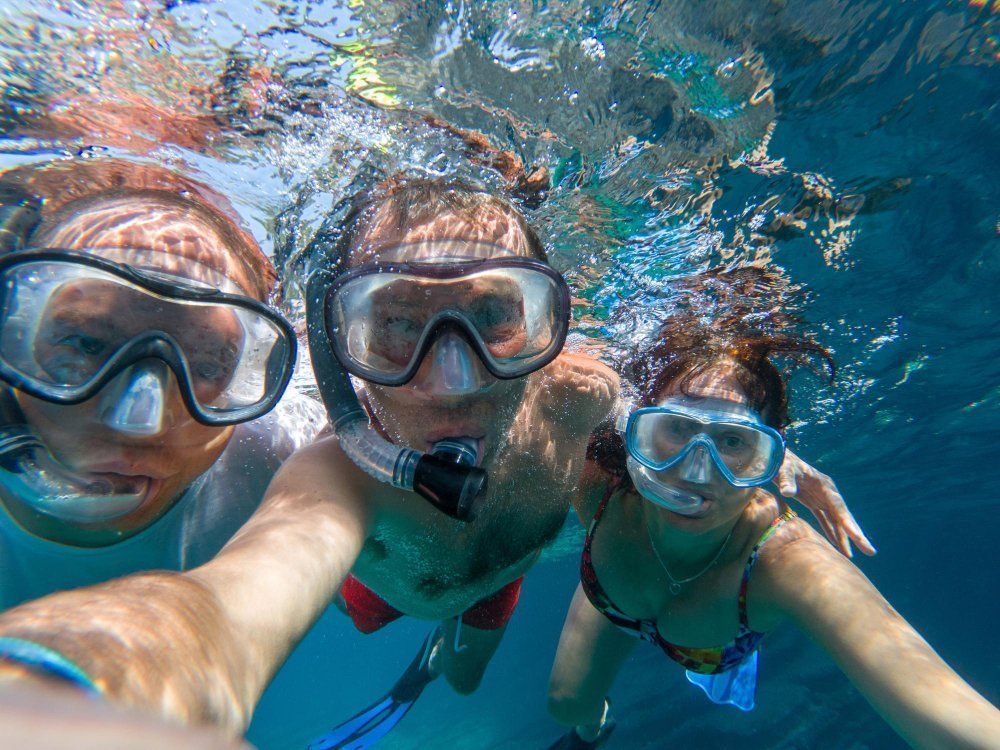 Familia buceando en aguas cristalinas durante un viaje de turismo de submarinismo con niños, disfrutando de peces tropicales y arrecifes.